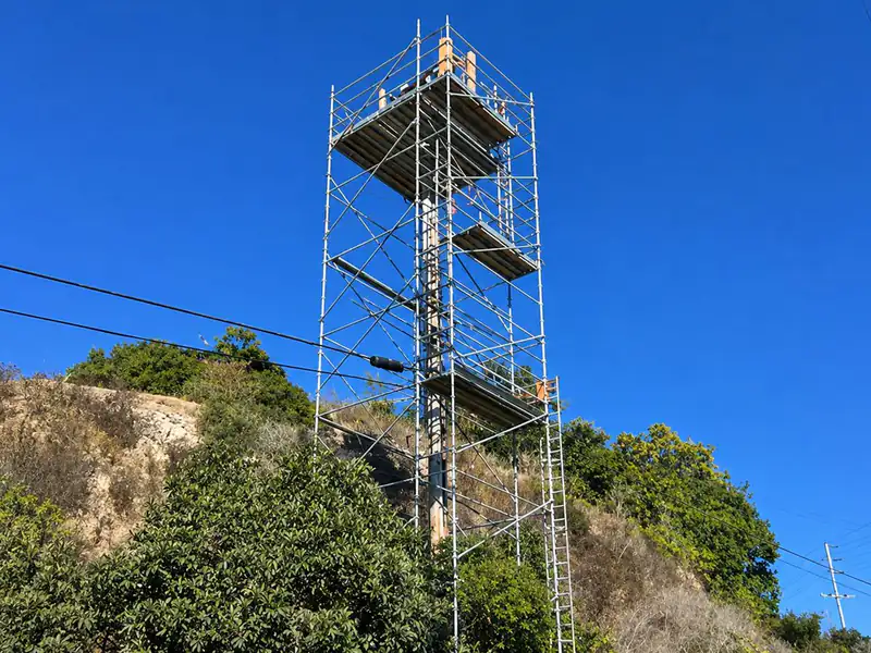 Tall scaffold tower with a top platform standing on a hillside against a blue sky